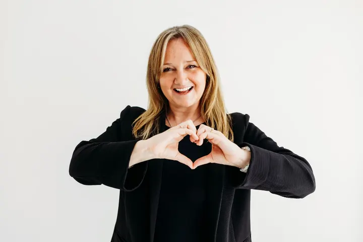 Emma Kneale smiling and making a heart shape with her hands