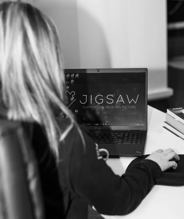 Woman working at a laptop showing the Jigsaw logo, seen from behind