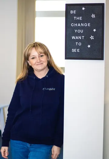 Emma Kneale in the Jigsaw office beside a letter board reading "Be the change you want to see"