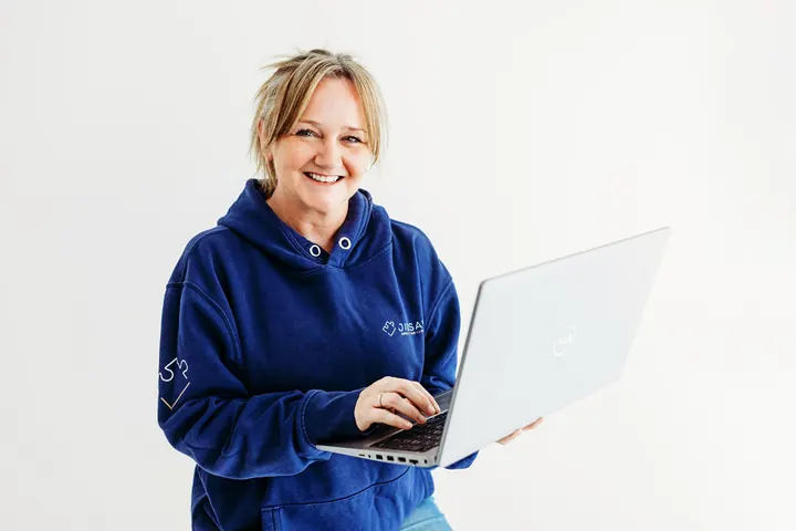 Emma Kneale smiling while working on a laptop in a Jigsaw hoodie